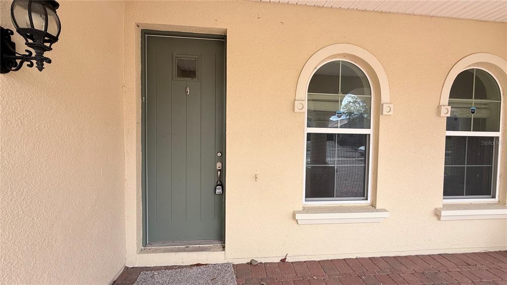 A green front door with a small window sits beside two arched windows on stucco — 3879 SHORESIDE DRIVE, KISSIMMEE, FL
