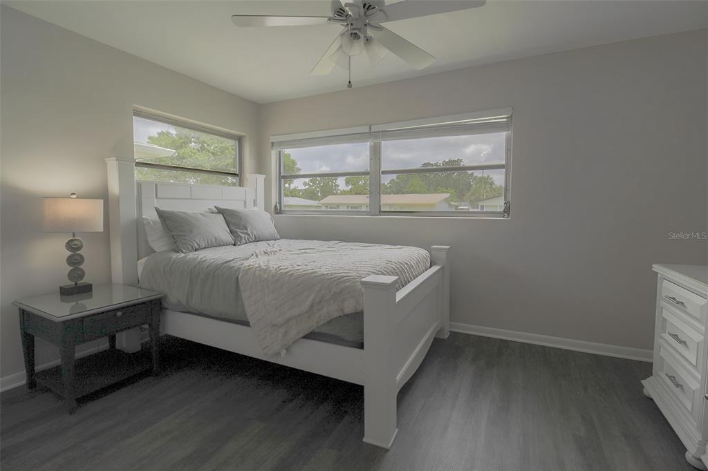 A bedroom features a white bed frame, gray bedding, a nightstand, and gray wood flooring — 2338 NASH STREET, CLEARWATER, FL