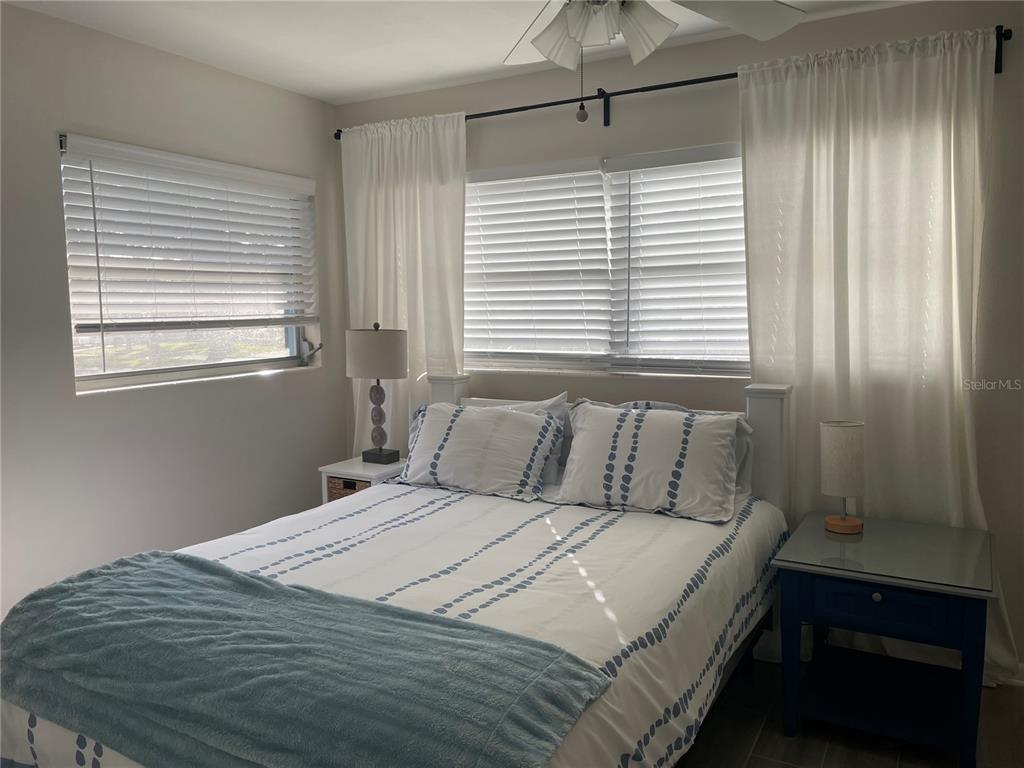 A bedroom features a bed with patterned bedding, two nightstands, and windows with white blinds — 2338 NASH STREET, CLEARWATER, FL