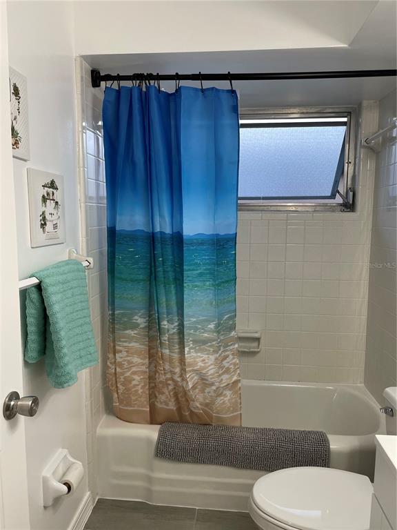 A bathroom features a white tiled bathtub, a beach-themed shower curtain, and a toilet — 2338 NASH STREET, CLEARWATER, FL