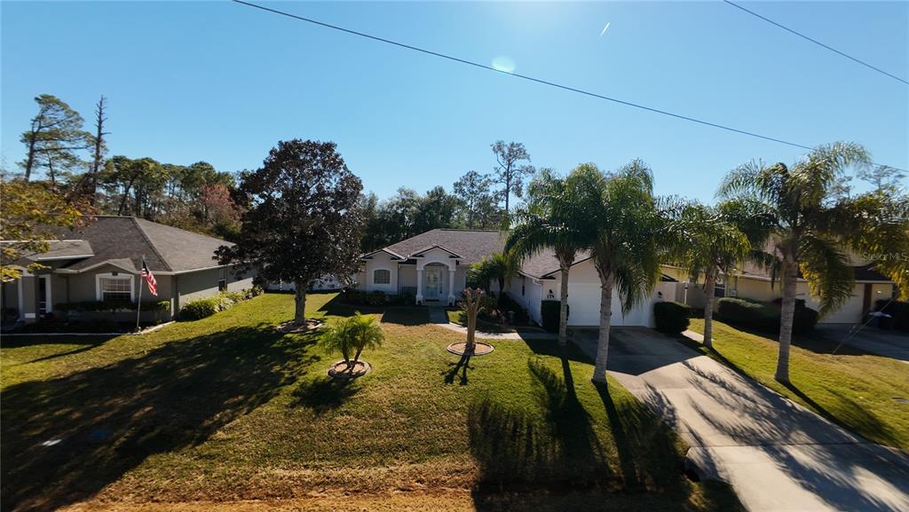 A single-story suburban house with a lawn, palm trees, and a concrete driveway — 114 FOXHALL LANE, PALM COAST, FL