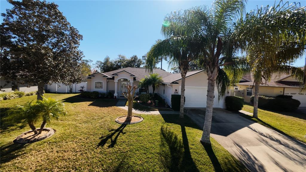 A single-story house with a white garage, a palm tree, and a grassy front yard — 114 FOXHALL LANE, PALM COAST, FL