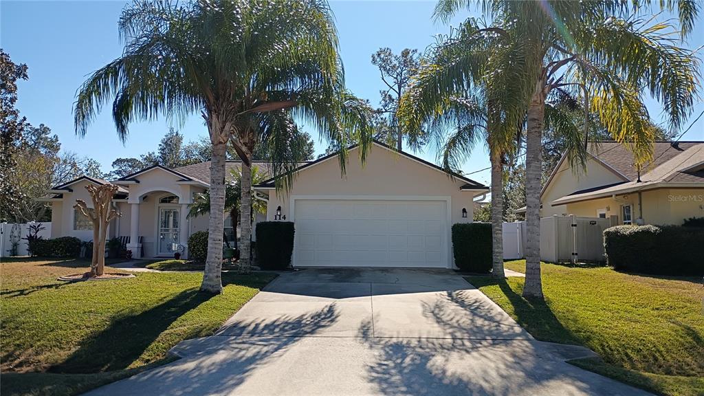 A single-story house with a two-car garage, palm trees, and a concrete driveway — 114 FOXHALL LANE, PALM COAST, FL