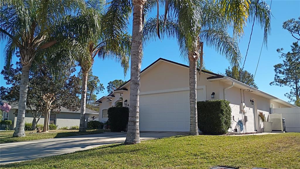 A single-story house with a white garage door and palm trees in the front yard — 114 FOXHALL LANE, PALM COAST, FL