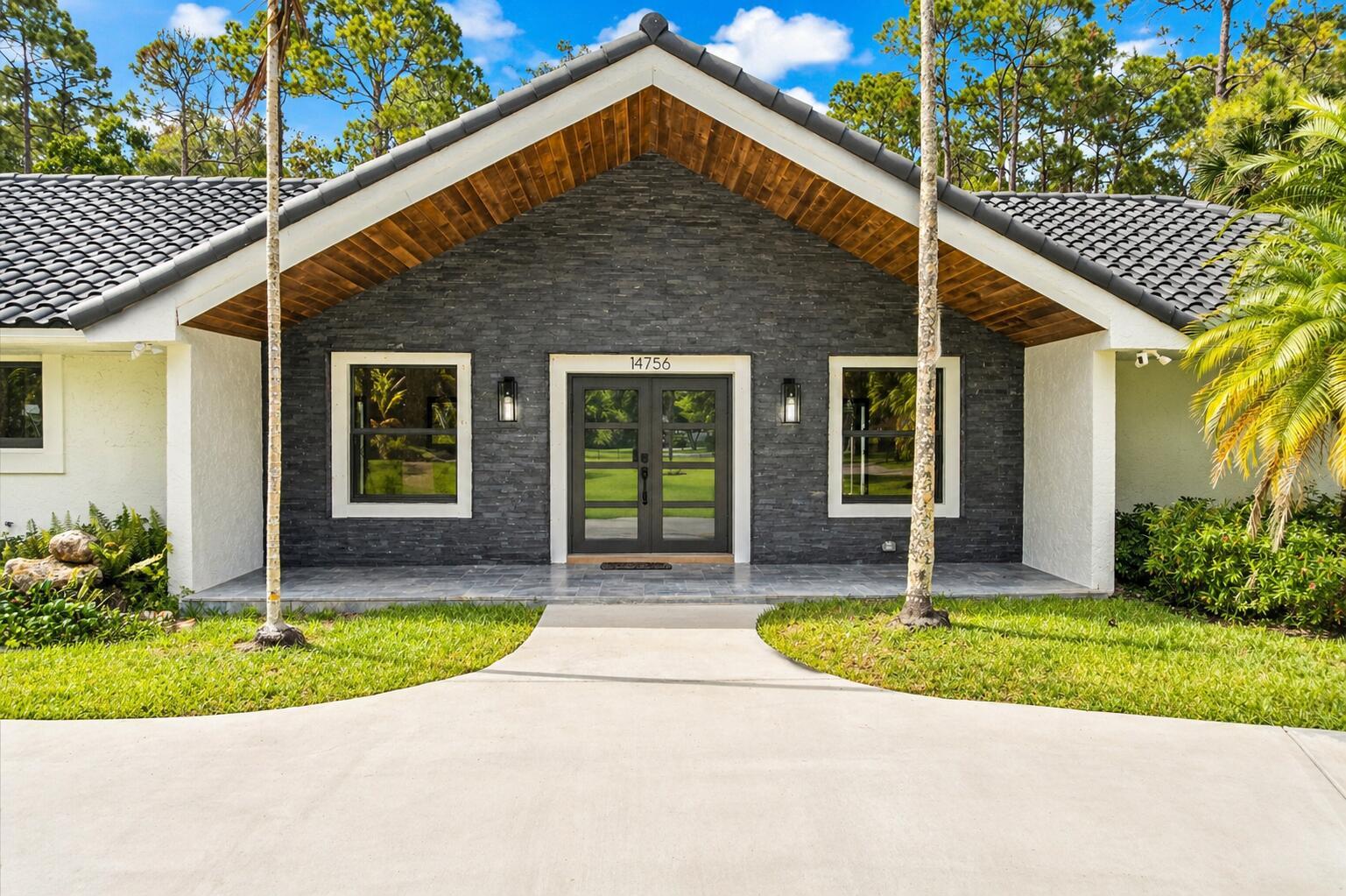 The front exterior of a house features a stone facade, double doors, and a gabled roof — 14756 Stirrup Lane, Wellington FL 33414, WELLINGTON, FL