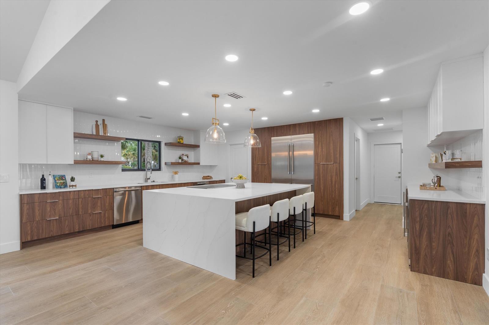 A modern kitchen features a large white quartz island, wood cabinetry, and stainless steel appliances — 14756 Stirrup Lane, Wellington FL 33414, WELLINGTON, FL
