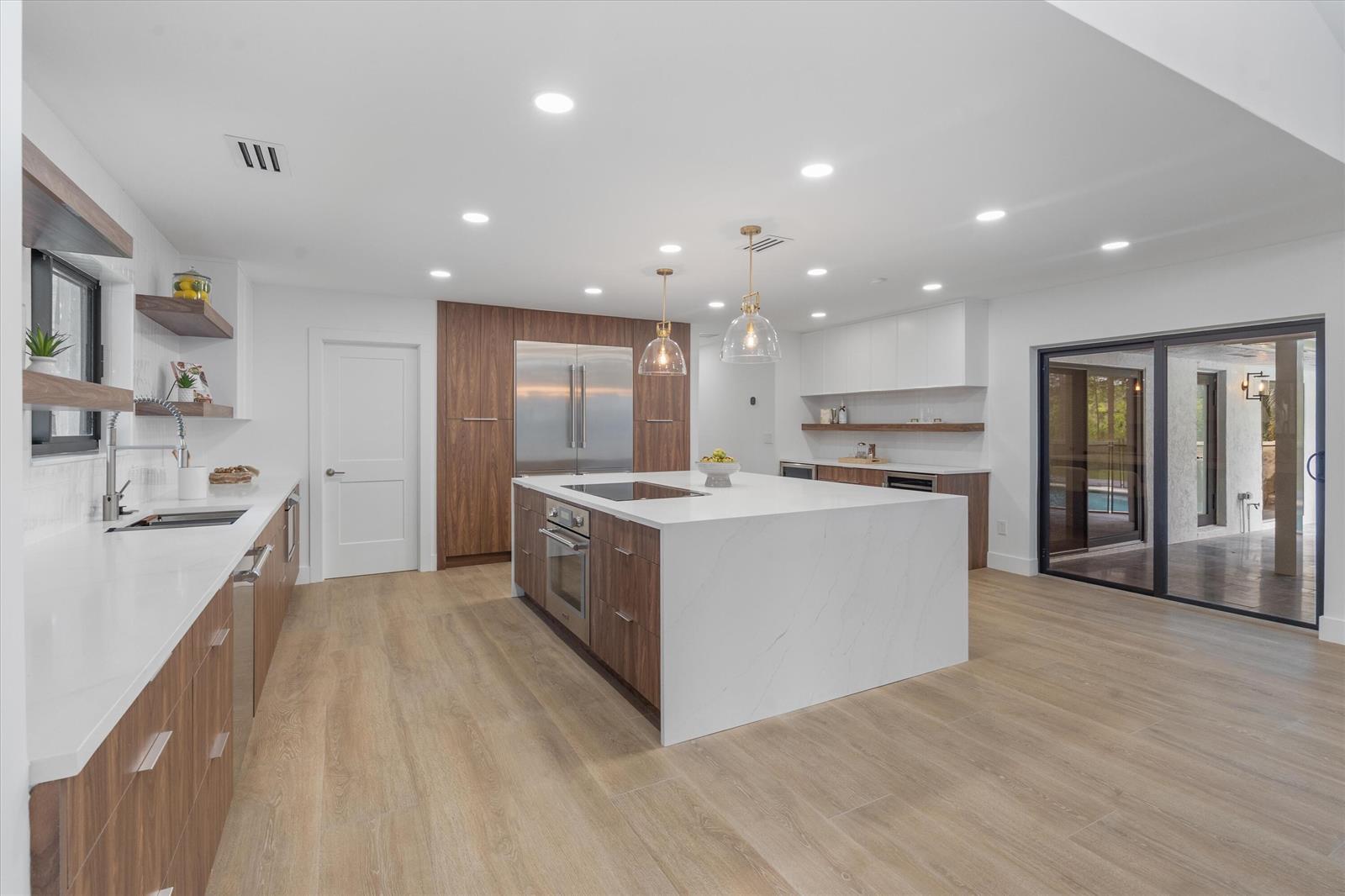 A modern kitchen features wood-toned cabinetry, a large white quartz island, and light wood flooring — 14756 Stirrup Lane, Wellington FL 33414, WELLINGTON, FL