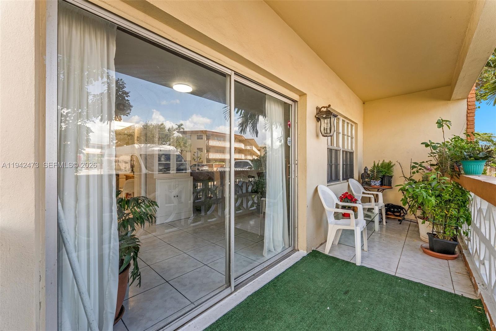 A covered balcony features tiled flooring, a green rug, white chairs, and several potted plants — 11840 NE 19th Dr # 9, North Miami FL 33181, NORTH MIAMI, FL