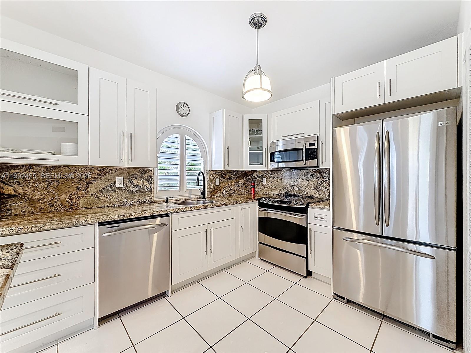A kitchen with white cabinets, granite countertops, and a central island overlooks a living area — 9008 Collins Ave # 303, Surfside FL 33154, SURFSIDE, FL