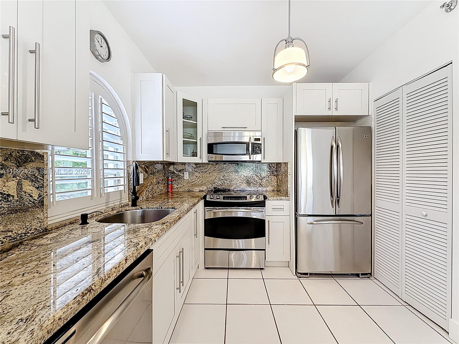 A kitchen features a stainless steel refrigerator, a stacked washer and dryer, and tiled flooring — 9008 Collins Ave # 303, Surfside FL 33154, SURFSIDE, FL