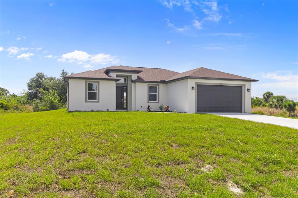 A single-story house with a white stucco exterior, a dark garage door, and a grassy yard — 7329 ATHENS TERRACE, PORT CHARLOTTE, FL