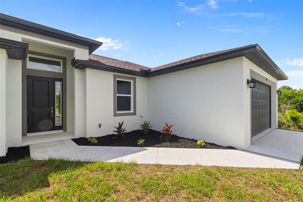 The exterior of a modern house features a dark front door, garage, and landscaping — 7329 ATHENS TERRACE, PORT CHARLOTTE, FL