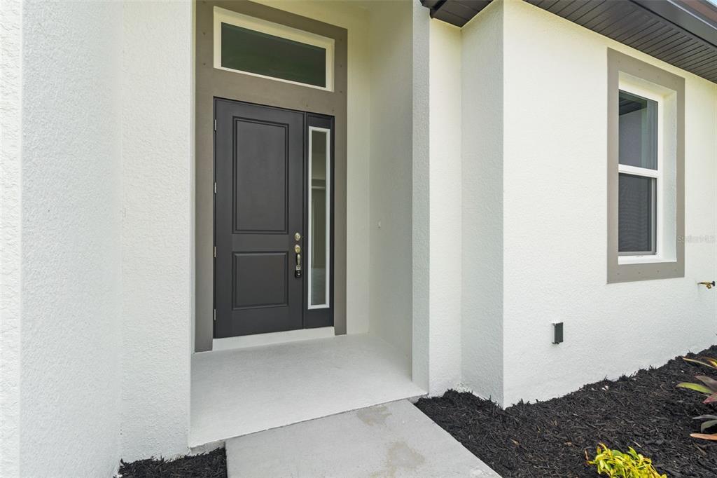 A modern front entryway features a dark gray door with a side light and transom window — 7329 ATHENS TERRACE, PORT CHARLOTTE, FL