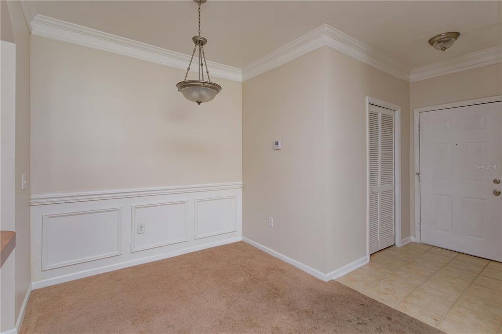 A dining area features beige carpet, wainscoting, a hanging light fixture, and an adjacent entryway — 12849 MADISON POINT CIRCLE UNIT 201, ORLANDO, FL
