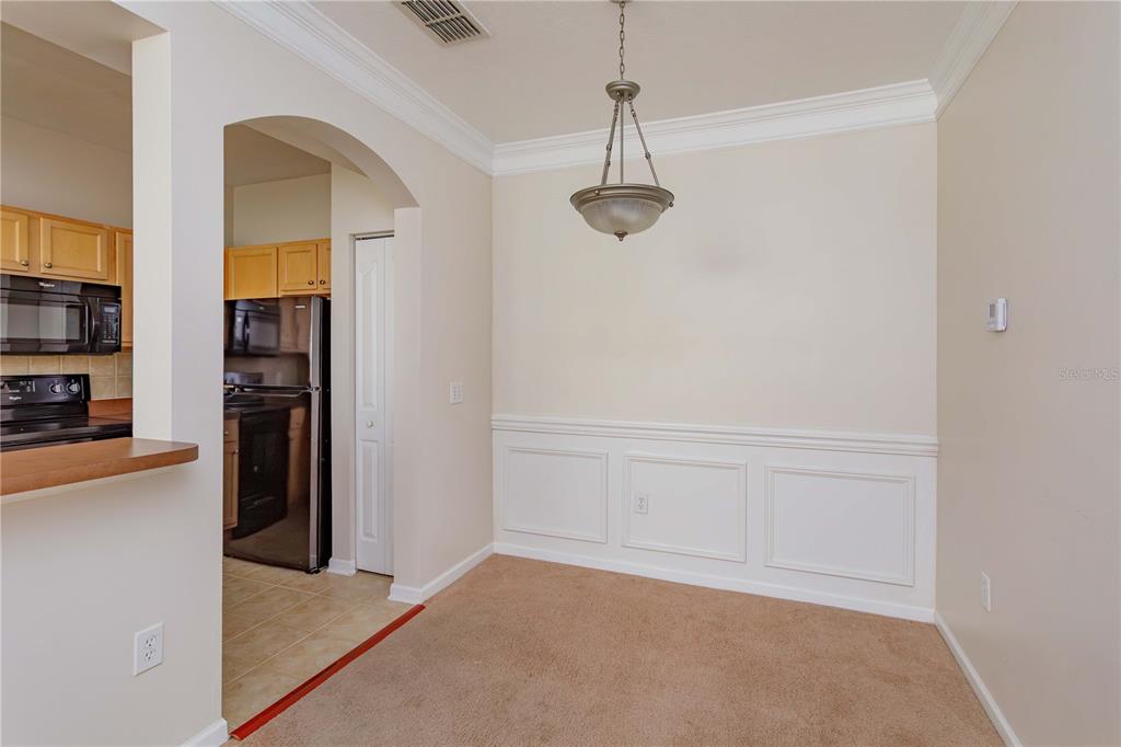 A dining area with beige carpet, white wainscoting, and a hanging pendant light fixture — 12849 MADISON POINT CIRCLE UNIT 201, ORLANDO, FL