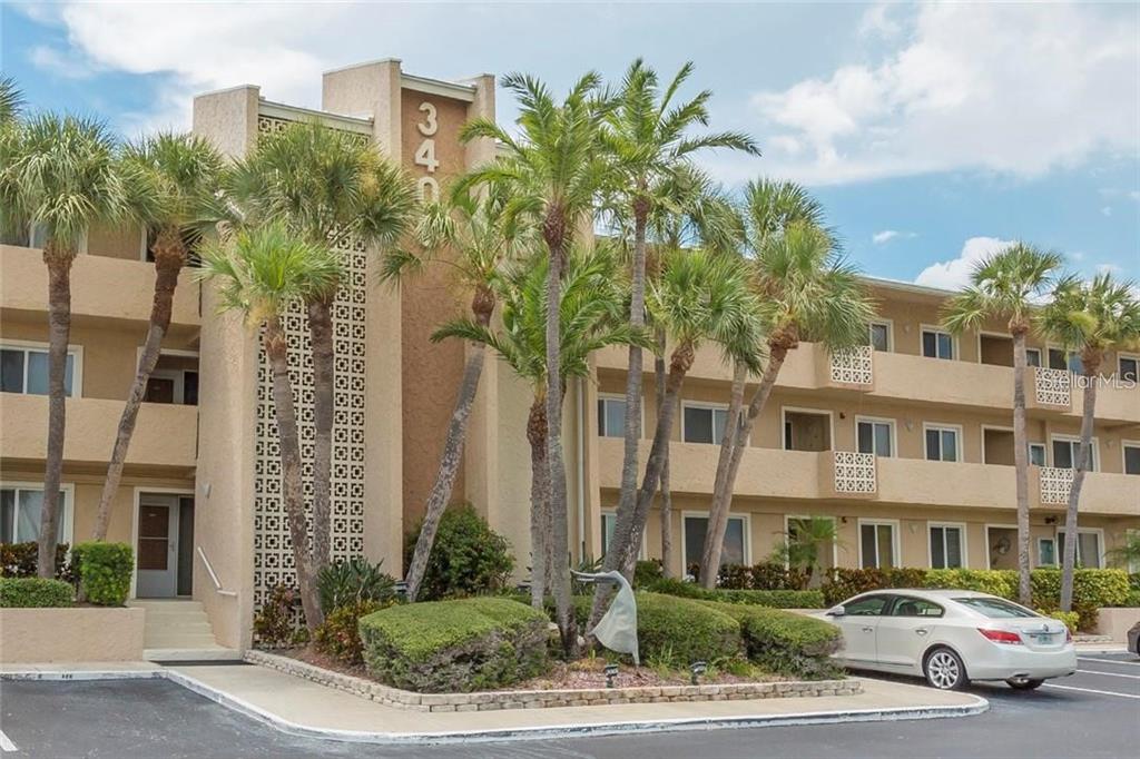 A three-story tan apartment building with palm trees and a parking lot in front — 3400 GULF BOULEVARD UNIT 201, BELLEAIR BEACH, FL