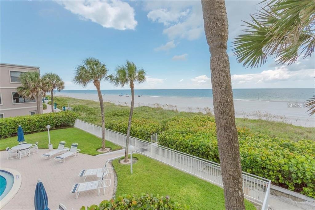 An elevated view of a beachside patio with lounge chairs, palm trees, and ocean access — 3400 GULF BOULEVARD UNIT 201, BELLEAIR BEACH, FL