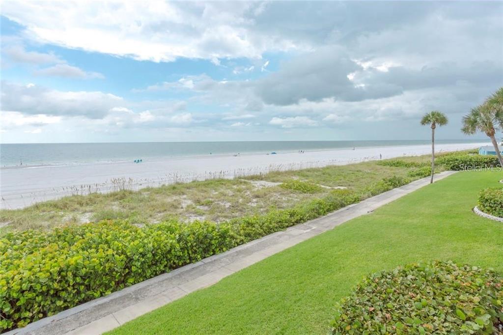 A view of a sandy beach and ocean from a grassy lawn with a walkway — 3400 GULF BOULEVARD UNIT 201, BELLEAIR BEACH, FL