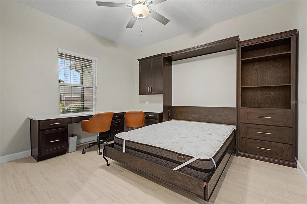 A room features a dark wood Murphy bed, built-in desk, shelving, and light tile flooring — 10460 GABLE DIG LOOP, SAN ANTONIO, FL