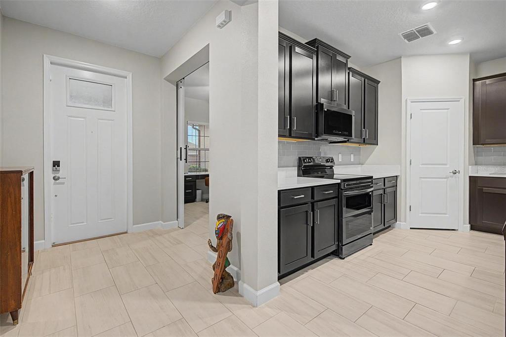 A kitchen with dark cabinets and light tile flooring opens to an entryway and office — 10460 GABLE DIG LOOP, SAN ANTONIO, FL