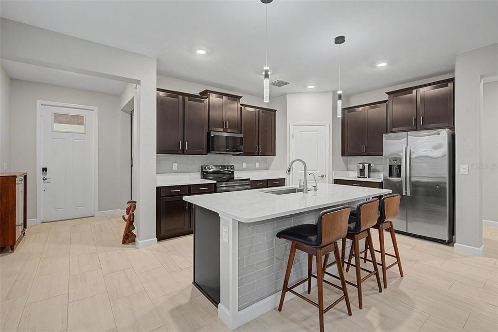 A modern kitchen features dark wood cabinets, white countertops, a central island, and three barstools — 10460 GABLE DIG LOOP, SAN ANTONIO, FL