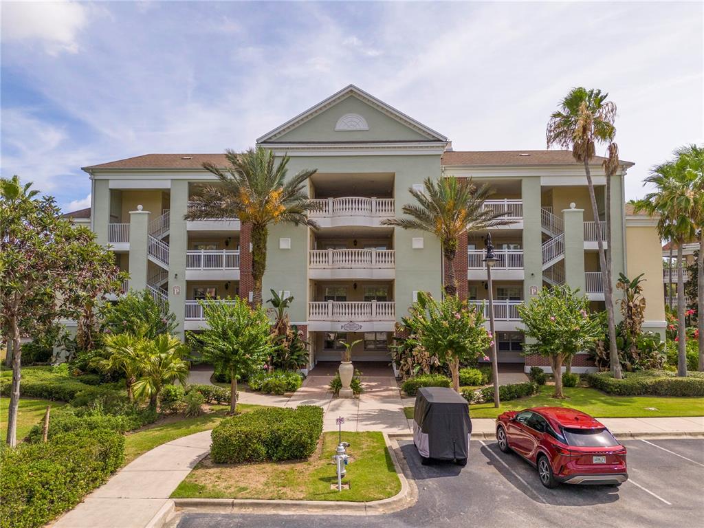 A three-story apartment building with a central entrance, balconies, and palm trees in the foreground — 7659 WHISPER WAY UNIT 304, REUNION, FL