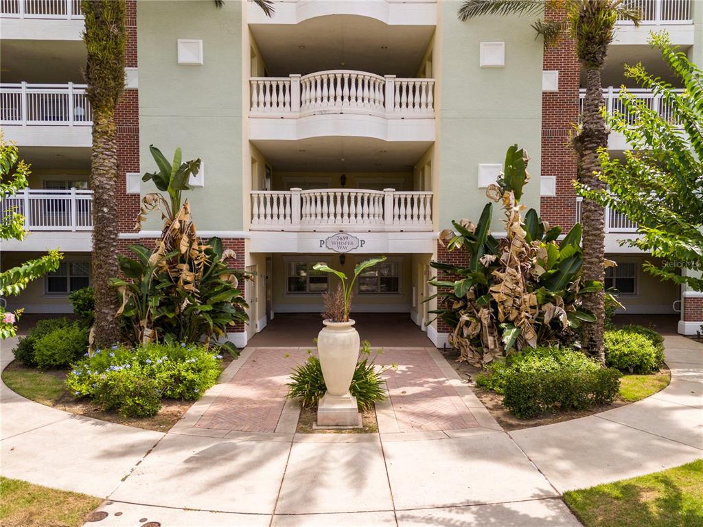 A multi-story apartment building exterior features balconies, a central walkway, and large potted plants — 7659 WHISPER WAY UNIT 304, REUNION, FL