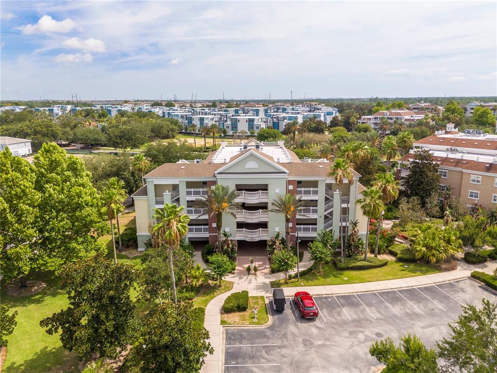An aerial view shows a multi-story residential building with a parking lot and landscaping — 7659 WHISPER WAY UNIT 304, REUNION, FL