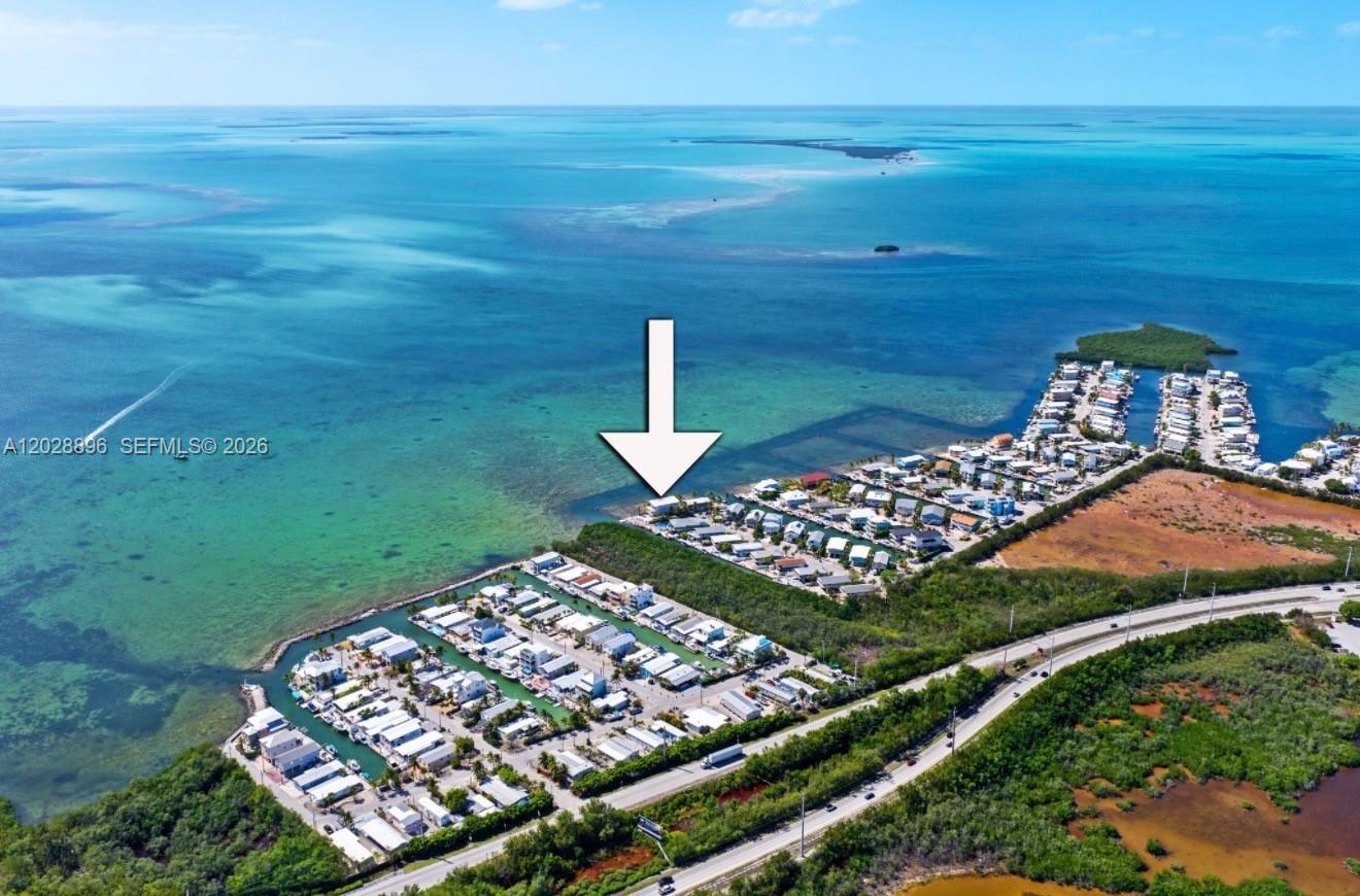 An aerial view shows a coastal residential community with a white arrow pointing toward a waterfront home — 233 Aberdeen Ct, Tavernier FL 33070, TAVERNIER, FL