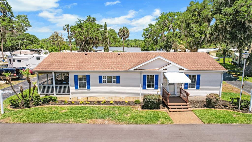 A single-story house with light siding, blue shutters, and a screened porch faces a lake — 15 RIVERVIEW DRIVE, FRUITLAND PARK, FL