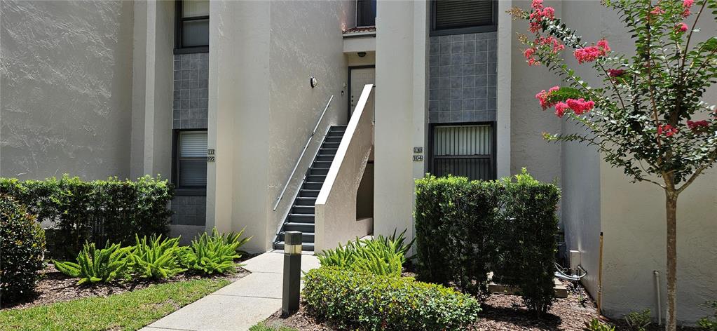 A two-story apartment building exterior features a central staircase, beige stucco walls, and landscaping — 105 LAUREL COVE WAY UNIT 105, WINTER HAVEN, FL