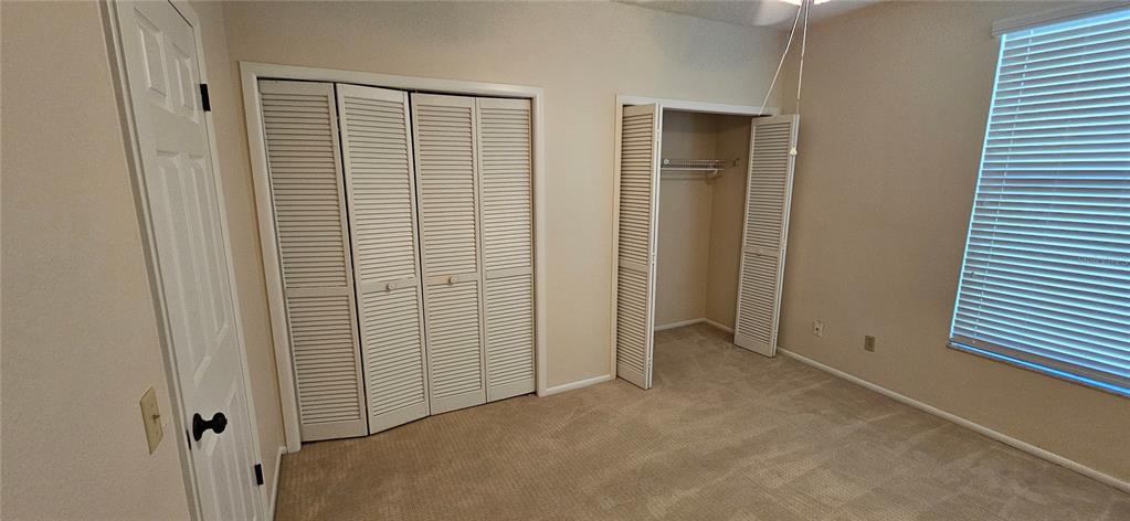 A bedroom features beige carpet, neutral walls, two louvered-door closets, and a window with blinds — 105 LAUREL COVE WAY UNIT 105, WINTER HAVEN, FL