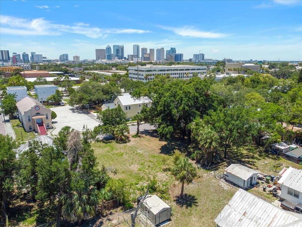 An aerial view shows a vacant lot with trees and surrounding buildings near a city skyline — 940 E 11TH AVENUE, TAMPA, FL
