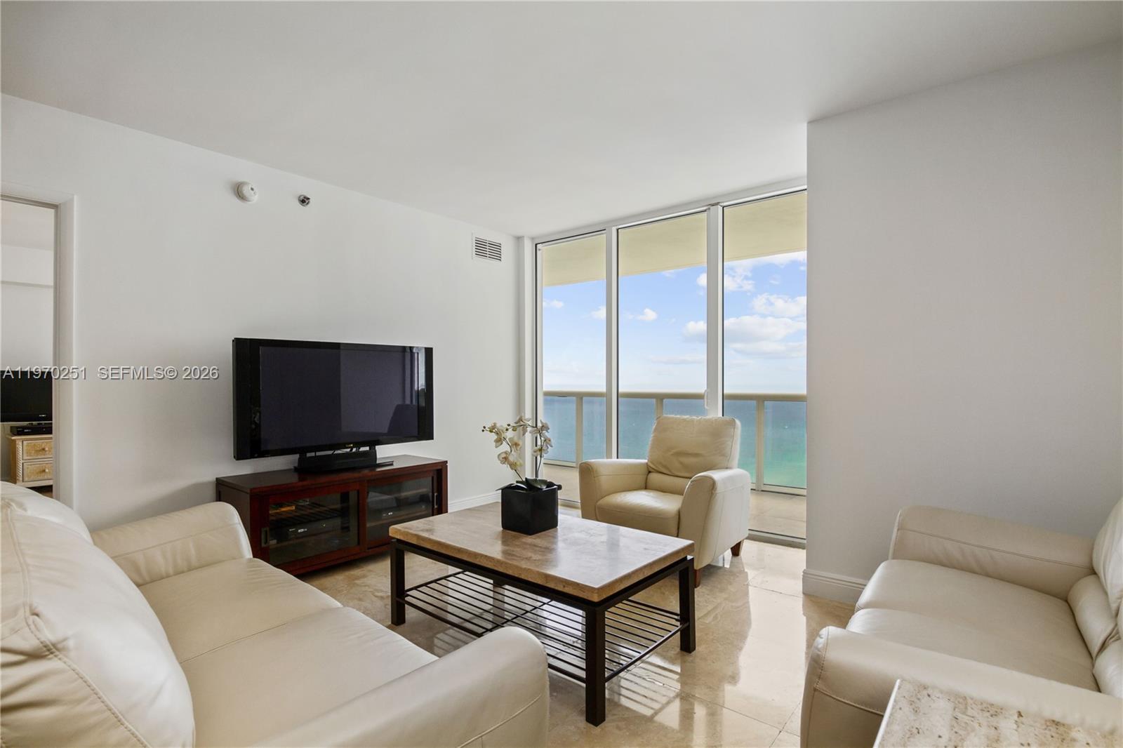 A living room features white leather sofas, a coffee table, and floor-to-ceiling ocean views — 1830 S Ocean Dr # 4204, Hallandale Beach FL 33009, HALLANDALE BEACH, FL