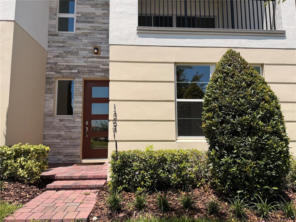 A modern townhouse exterior features a stone-accented entryway, a brown door, and a large bush — 13641 LARKTON LANE, ORLANDO, FL