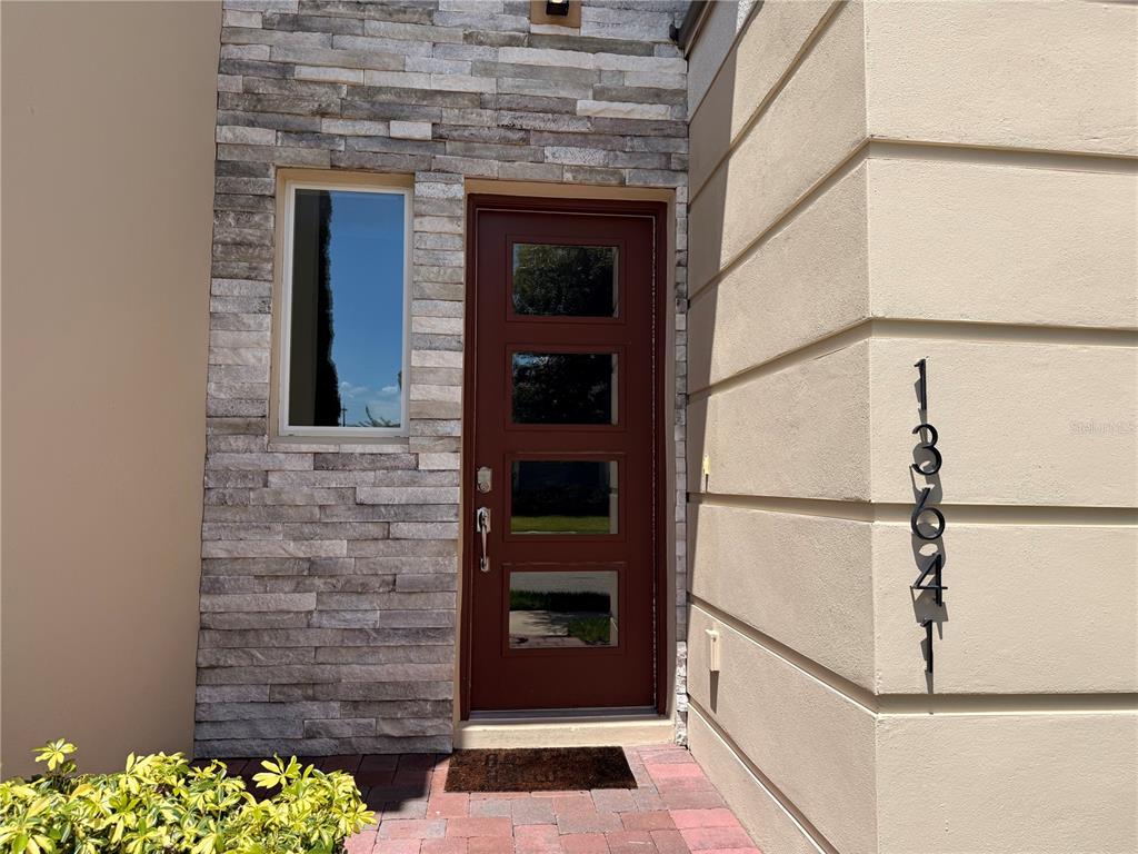 A modern front entrance features a brown door, stone veneer siding, and vertical house numbers — 13641 LARKTON LANE, ORLANDO, FL