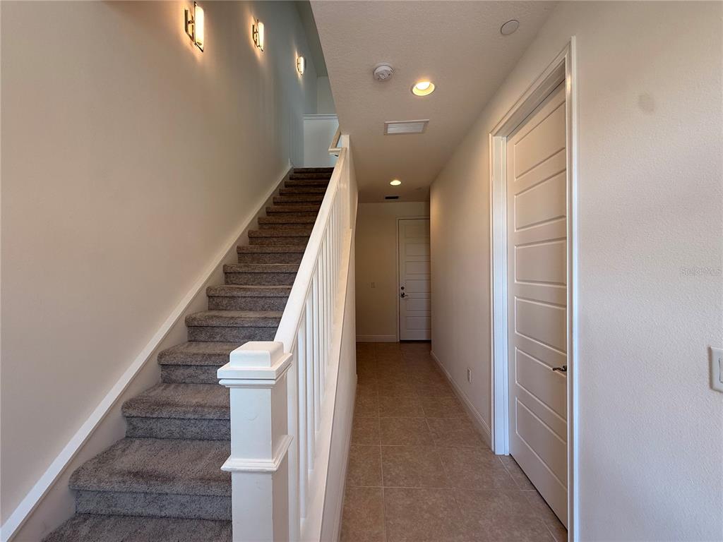 A carpeted staircase with a white railing sits beside a tiled hallway with two doors — 13641 LARKTON LANE, ORLANDO, FL