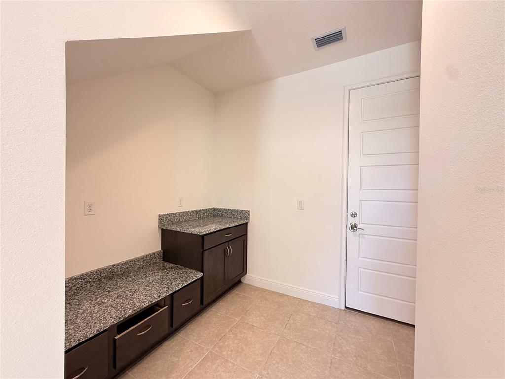 A laundry room features dark wood cabinets, granite countertops, and a white paneled door — 13641 LARKTON LANE, ORLANDO, FL