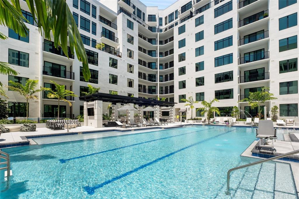 A large swimming pool sits in the courtyard of a multi-story white apartment building — 1991 MAIN STREET Aster - B4, SARASOTA, FL