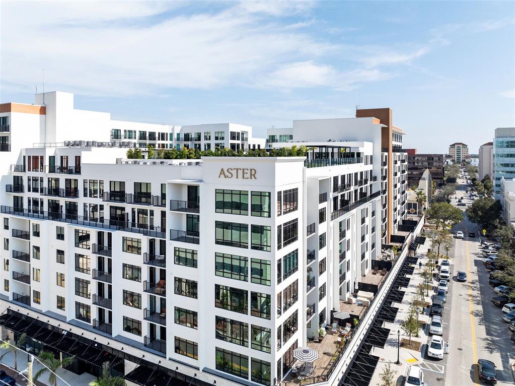 An aerial view shows the exterior of a modern white apartment building named Aster — 1991 MAIN STREET Aster - B4, SARASOTA, FL