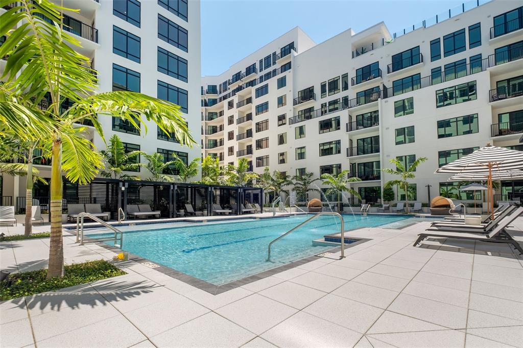 A swimming pool with lounge chairs and cabanas sits in the courtyard of a modern apartment — 1991 MAIN STREET Aster - B4, SARASOTA, FL