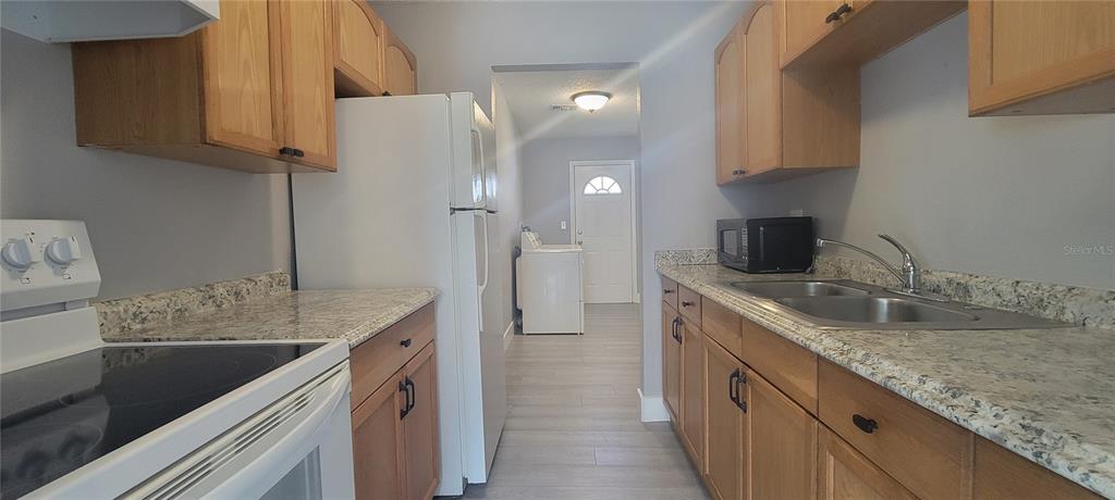 A kitchen with light wood cabinets, granite countertops, and a white refrigerator leads to a laundry area — 6625 S WEST SHORE BOULEVARD, TAMPA, FL