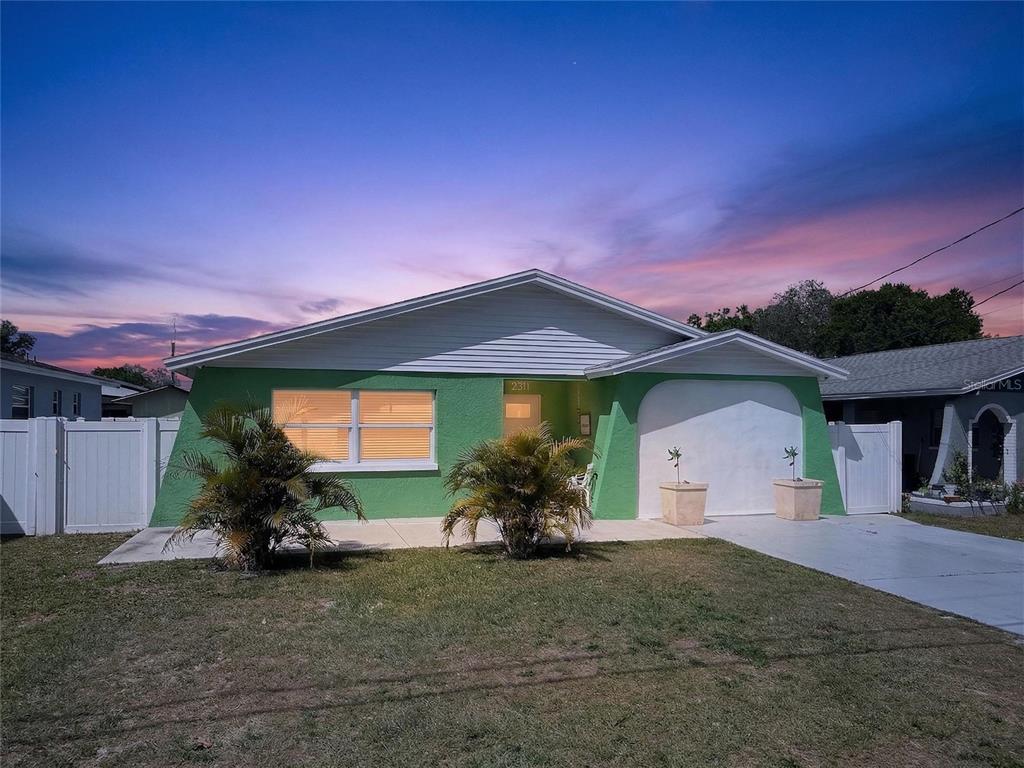 A green single-story house with a white garage and a front yard at dusk — 2311 W KENTUCKY AVENUE, TAMPA, FL