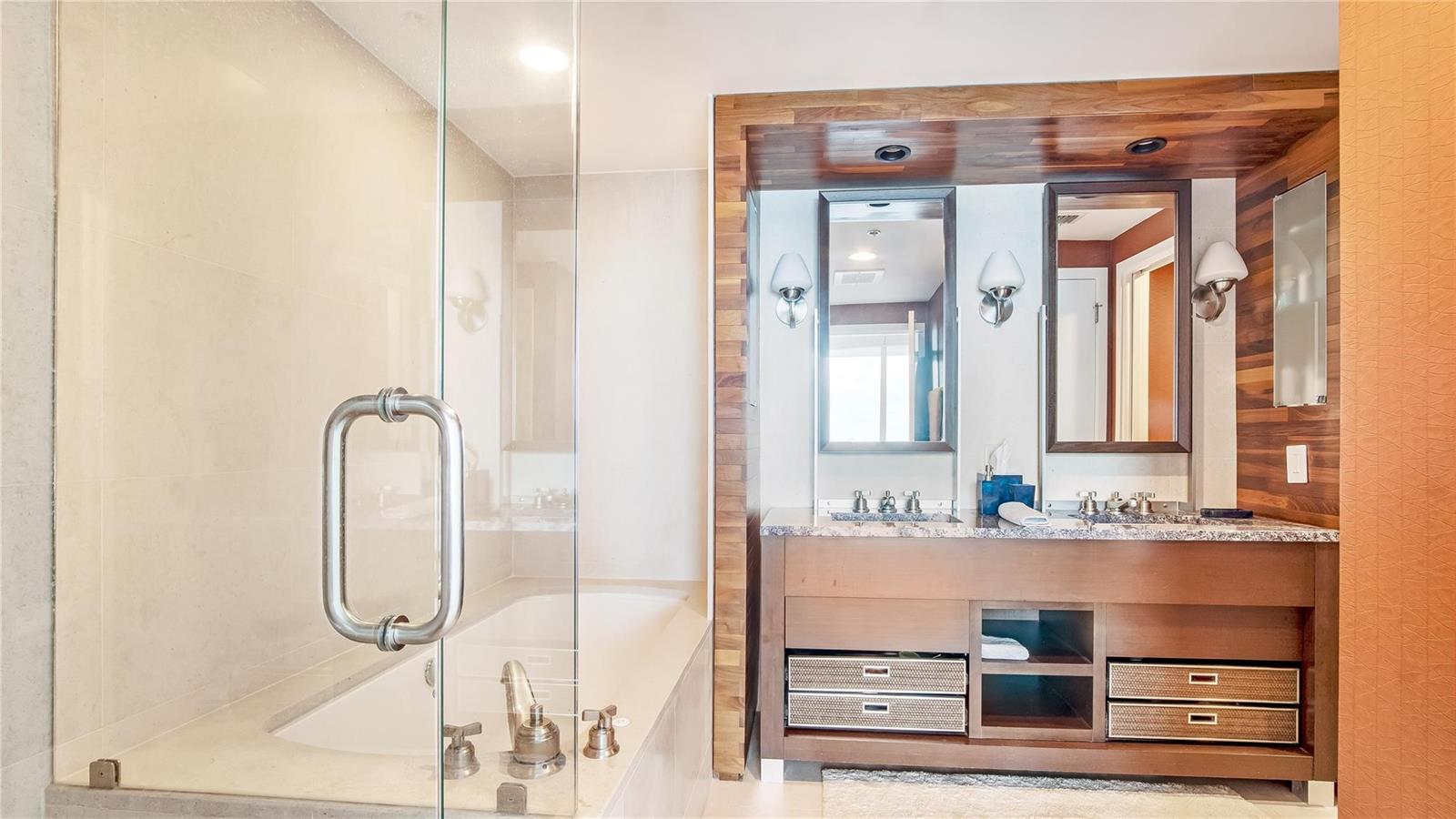 A bathroom features a glass-enclosed shower and tub area next to a wooden double vanity — 6899 Collins Avenue # 1203, Miami Beach FL 33141, MIAMI BEACH, FL