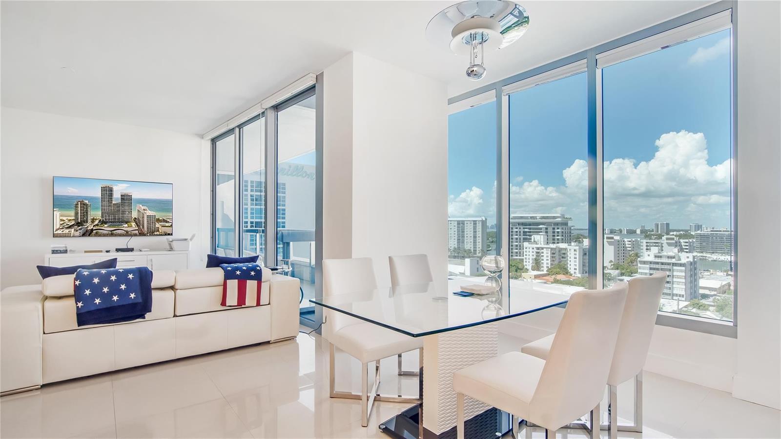 A bright living and dining area with white furniture, a glass table, and floor-to-ceiling windows — 6899 Collins Avenue # 1203, Miami Beach FL 33141, MIAMI BEACH, FL