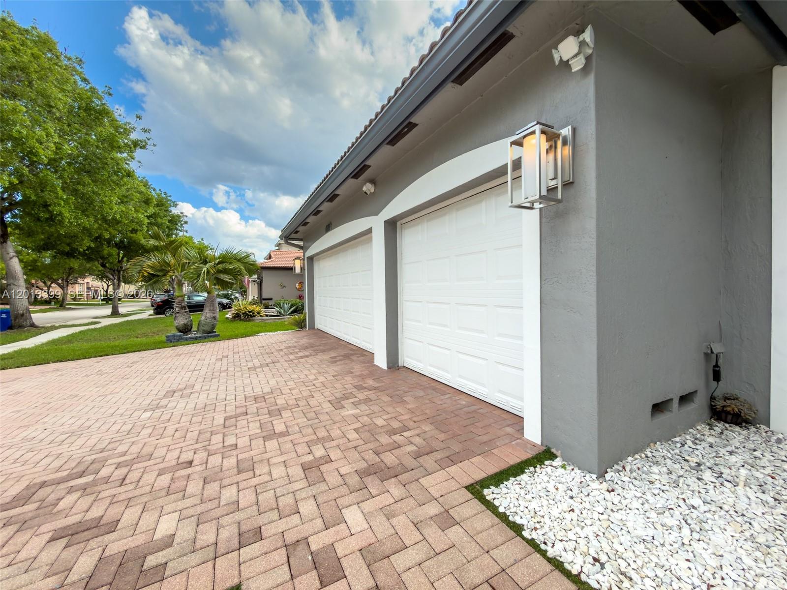 A gray house exterior features two white garage doors and a brick paver driveway — 5312 SW 148th Ave, Miramar FL 33027, MIRAMAR, FL