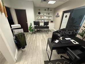 An office space features two black desks, light wood-look flooring, and white floating shelves — 13574 VILLAGE PARK DRIVE UNIT GE, ORLANDO, FL