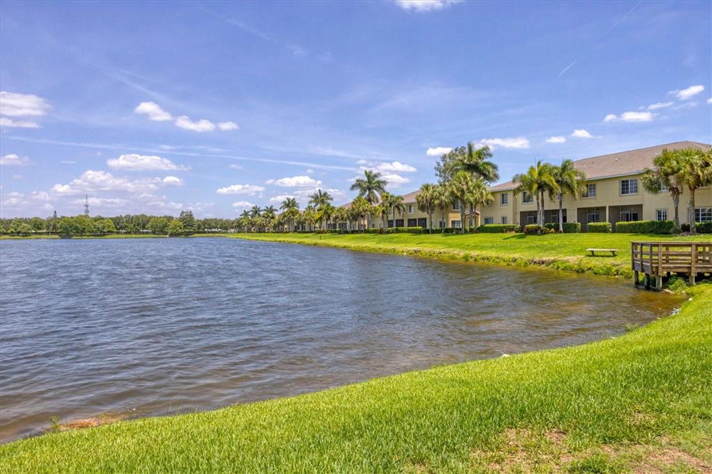A multi-story apartment building sits along a lake with palm trees and a wooden dock — 3603 45TH TERRACE W UNIT 101, BRADENTON, FL