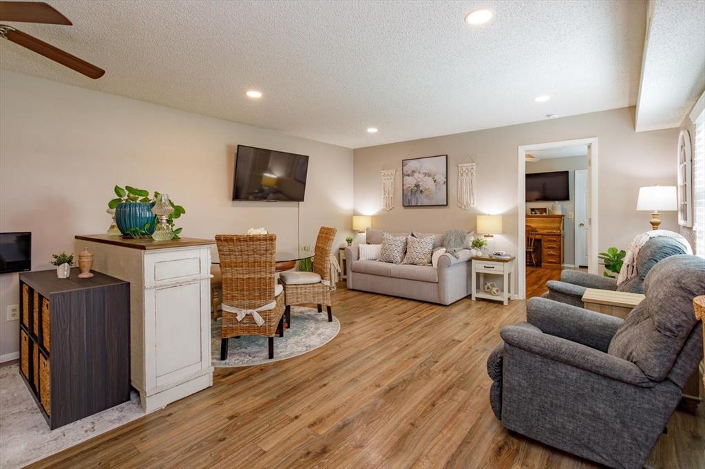 A living and dining area features wood-look flooring, a gray sofa, and two recliner chairs — 27 WINDTREE LANE UNIT 102, WINTER GARDEN, FL