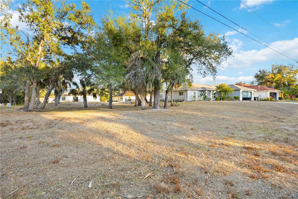 A grassy, tree-filled vacant lot sits in front of several suburban houses — Lot 26 HOLLAND STREET, NORTH PORT, FL